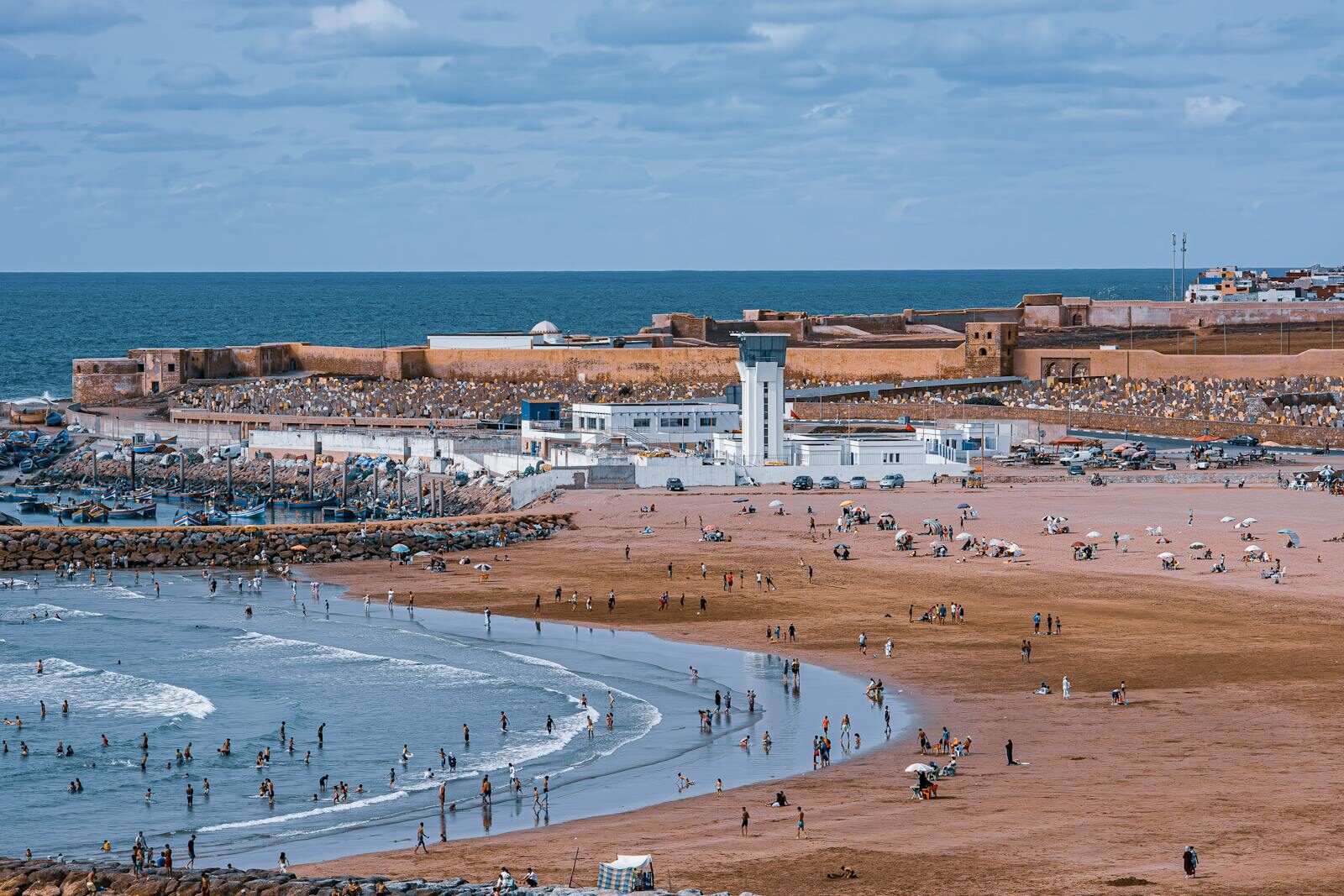 A vibrant beach scene near Rabat's historic fort with people enjoying sun and sea.