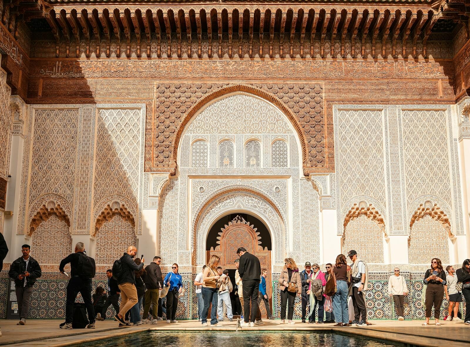 Group of tourists exploring Ben Youssef Madrasa's intricate architecture in sunny Marrakech.